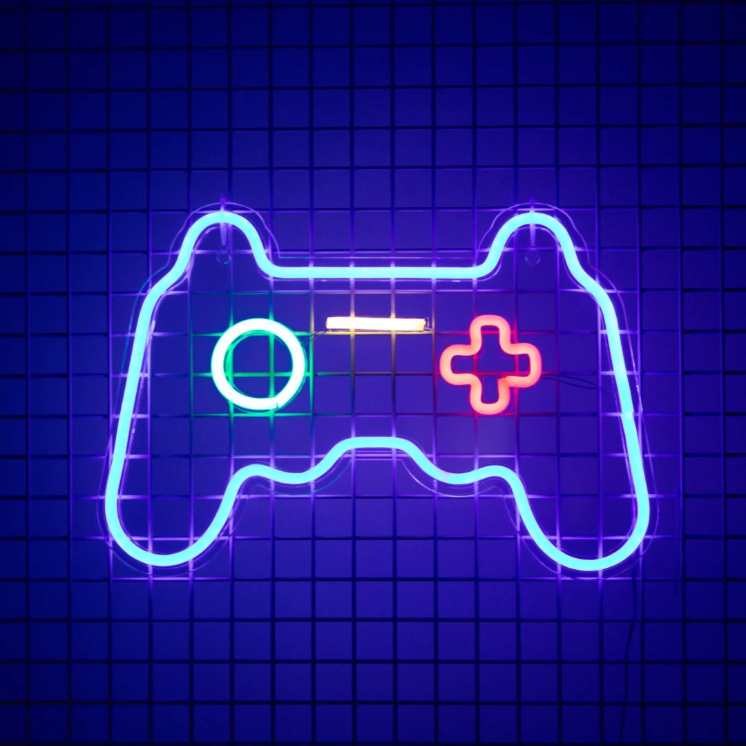 Neon Gamepad. Wielokolorowy neon w kształcie pada do gier wideo na ciemnym, kratkowanym tle. Jasne kolory neonu kontrastują z głębokim granatem tła, tworząc dynamiczny i futurystyczny efekt, idealny na eventy w stylu industrialnym czy nawiązujące do świata gier. Wrocławska wypożyczalnia dekoracji rent4events.pl oferuje unikalne rozwiązania na eventy, a rent4weddings.pl tworzy niezapomniane wspomnienia na weselach - rent4events.pl wypożycz wrażenia, rent4weddings.pl zachowaj wspomnienia.