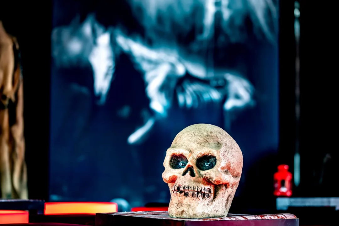 Zbliżenie na manekina z groteskową, zdeformowaną twarzą w halloweenowej scenografii. Widoczne szczegóły przerażającej maski z intensywnymi, krwawymi detalami. W tle mroczny wizerunek postaci szkieletu w kapturze, oświetlony światłem w niebieskiej tonacji. Idealna dekoracja na tematyczne eventy i imprezy grozy we Wrocławiu i okolicach. Dostępne w wypożyczalni Rent4Events.pl, która oferuje wyjątkowe dodatki na każdą okazję - rent4events.pl wypożycz wrażenia, rent4weddings.pl zachowaj wspomnienia. Fot. Marek Kaźmierczak @marekkazmierczak.