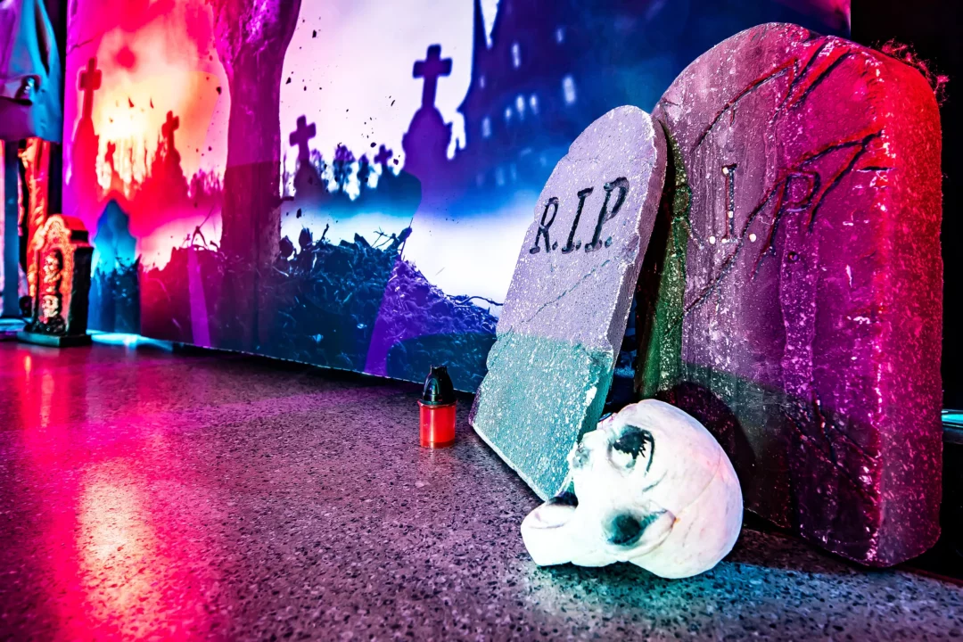 Dekoracja halloweenowa przedstawiająca nagrobki z napisem "R.I.P.", czaszkę oraz czerwony znicz, na tle cmentarza w świetle księżyca. Kolory fioletowe, różowe i czerwone tworzą tajemniczy, upiorny klimat, idealny na eventy tematyczne we Wrocławiu. Scenografia inspirowana grozą dostępna w wypożyczalni Rent4Events.pl, która oferuje unikalne dekoracje na specjalne okazje - rent4events.pl wypożycz wrażenia, rent4weddings.pl zachowaj wspomnienia. Fot. Marek Kaźmierczak @marekkazmierczak.