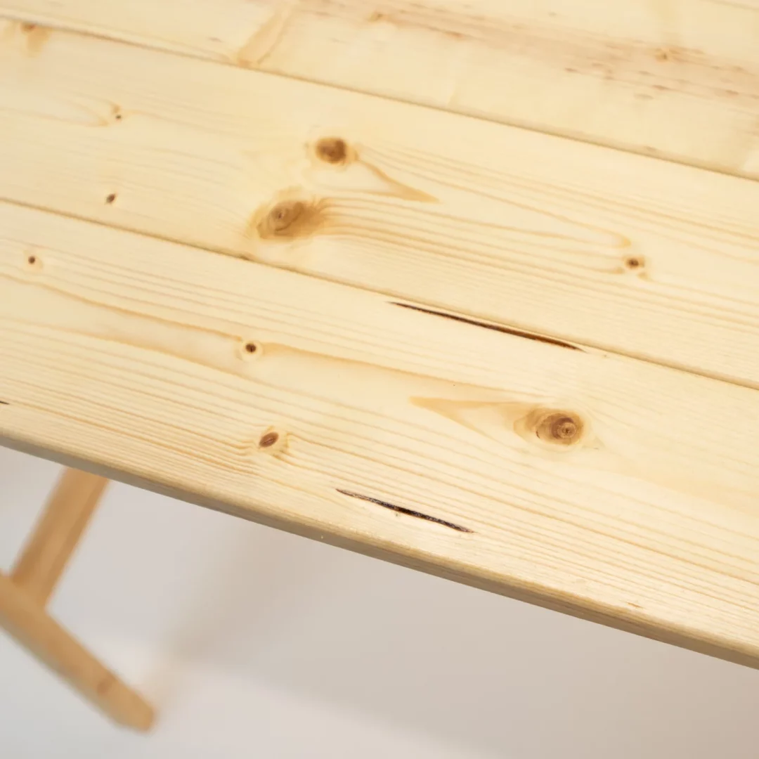 Zbliżenie na blat stołu z surowego, jasnego drewna z widocznymi słojami i sękami prezentuje jakość naturalnego materiału, idealnego na pikniki, do scenografii eventowej i stylowych aranżacji weselnych w wiejskim stylu. Tekstura drewna dodaje ciepła każdemu wydarzeniu, podkreślając charakter przyjęć plenerowych i ślubów w stylu rustykalnym. Wypożyczalnia dekoracji i mebli eventowych RENT4EVENTS – Wrocław - rent4events.pl wypożycz wrażenia, rent4wedding.pl zachowaj wspomnienia.