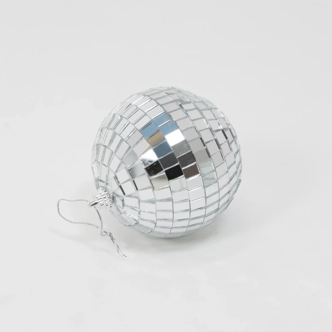 Kula Disco ⌀ 8. Srebrna kula dyskotekowa o średnicy 8 cm, pokryta lustrzanymi płytkami odbijającymi światło, idealna jako dekoracja na eventy w rytmach disco, inne muzyczne wydarzenia, wesela lub do wykorzystania w budowaniu scenografii. Jej elegancki i nowoczesny design sprawdzi się w każdej aranżacji, dodając blasku i tworząc niepowtarzalny klimat. Kula wyposażona jest w srebrny sznurek, co umożliwia jej łatwe zawieszenie. Idealna do wynajęcia we Wrocławiu (i nie tylko) z oferty Rent4Events.pl oraz Rent4Weddings.pl. To doskonałe rozwiązanie dla osób poszukujących efektownych dekoracji na różne okazje - rent4events.pl wypożycz wrażenia, rent4wedding.pl zachowaj wspomnienia.
