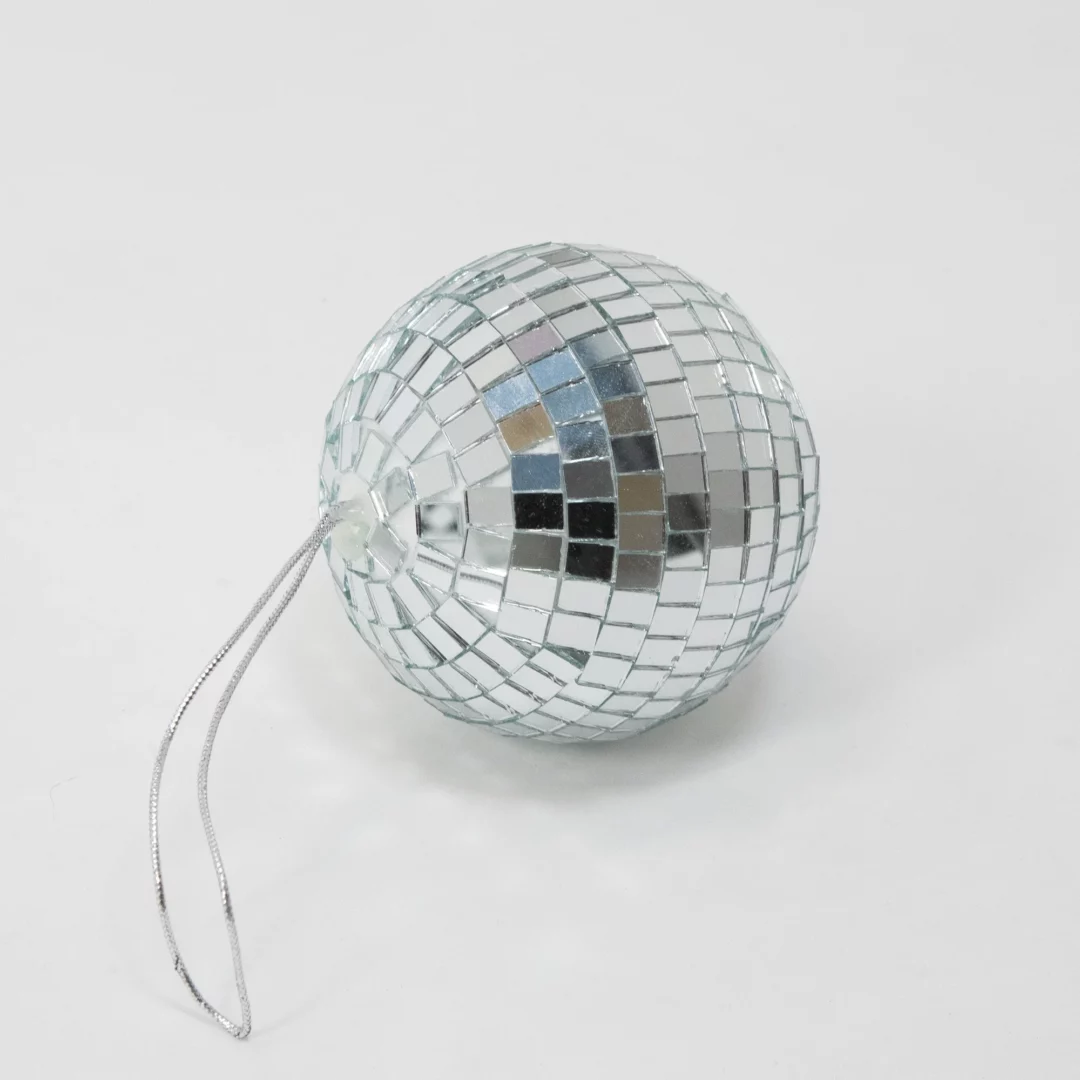 Kula Disco ⌀ 10. Srebrna kula dyskotekowa o średnicy 8 cm, pokryta lustrzanymi płytkami odbijającymi światło, idealna jako dekoracja na eventy w rytmach disco, inne muzyczne wydarzenia, wesela lub do wykorzystania w budowaniu scenografii. Jej elegancki i nowoczesny design sprawdzi się w każdej aranżacji, dodając blasku i tworząc niepowtarzalny klimat. Kula wyposażona jest w srebrny sznurek, co umożliwia jej łatwe zawieszenie. Idealna do wynajęcia we Wrocławiu (i nie tylko) z oferty Rent4Events.pl oraz Rent4Weddings.pl. To doskonałe rozwiązanie dla osób poszukujących efektownych dekoracji na różne okazje - rent4events.pl wypożycz wrażenia, rent4wedding.pl zachowaj wspomnienia.