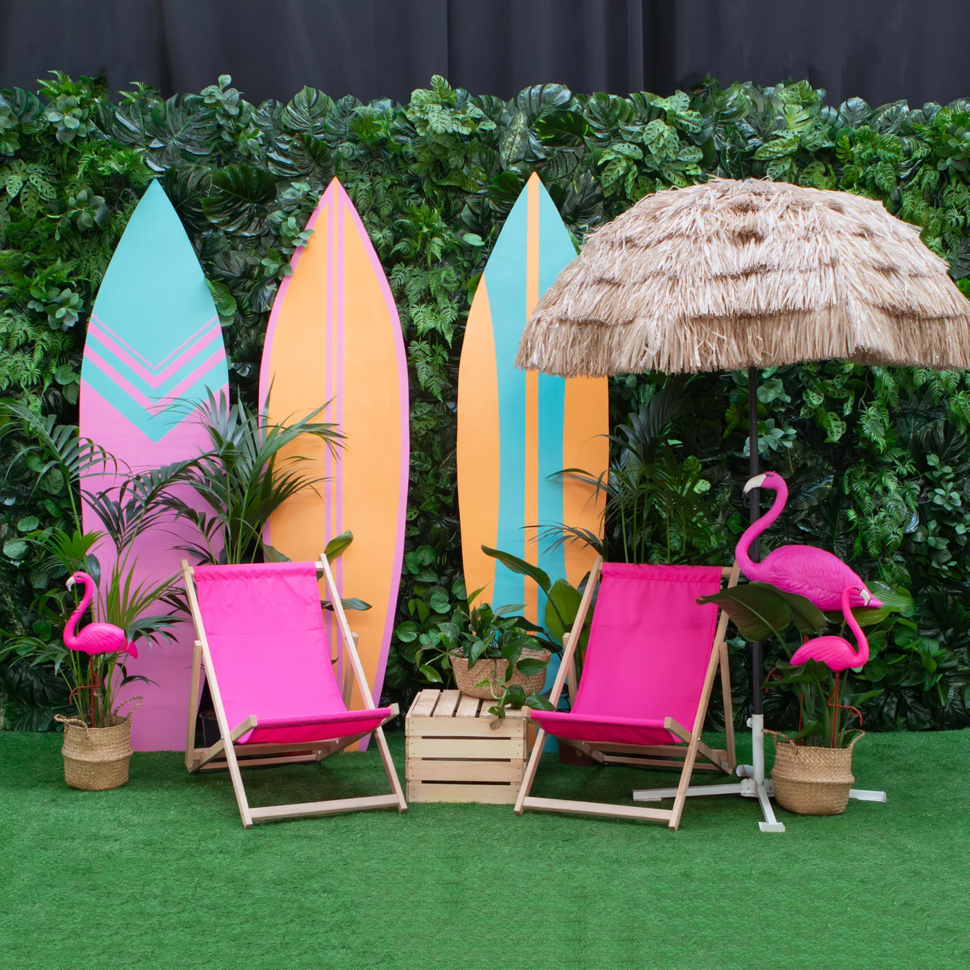 Profesjonalna scenografia "tropical beach" z deskami surfingowymi, flamingami oraz różowymi leżakami tworzy efektowne dekoracje premium na wydarzenia sezonowe. Dekoracje z parasola palmowego, różówych leżaków, stolika z drewnianej skrzynki, sztucznych roślin i flamingów ustawione są na tle ścianki tropikalne ze sztucznych roślin. Ta mała strefa chillout od wypożyczalnia dekoracji doskonale sprawdzi się podczas firmowego event, sesji zdjęciowej czy egzotycznego ślub. Zielona ściana, pastelowe kolory i naturalny parasol tiki podkreślają wakacyjny klimat oraz wysoką jakość aranżacji - rent4events.pl wypożycz wrażenia, rent4wedding.pl zachowaj wspomnienia.